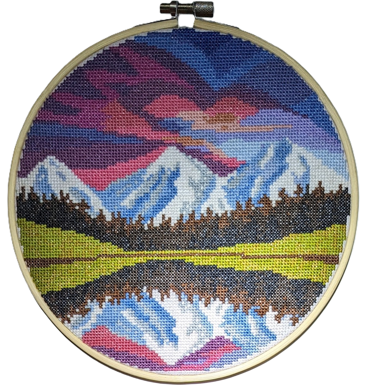 A finished cross-stitch project depicting a serene mountainscape with a colorful sky